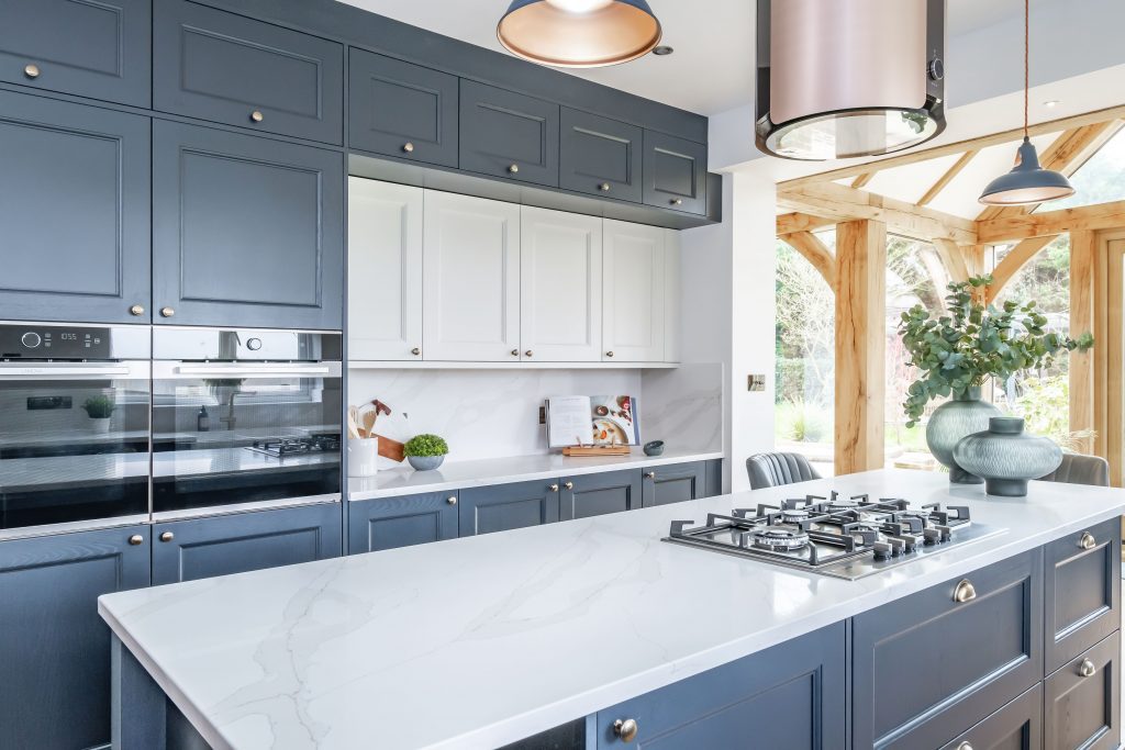 Luxury modern kitchen with navy shaker cabinets, white quartz island countertop, built-in double ovens, gas cooktop, and contemporary pendant lighting.