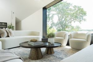 Modern minimalist living room with curved white sofas, textured cushions, and bronze coffee tables styled with books and greenery