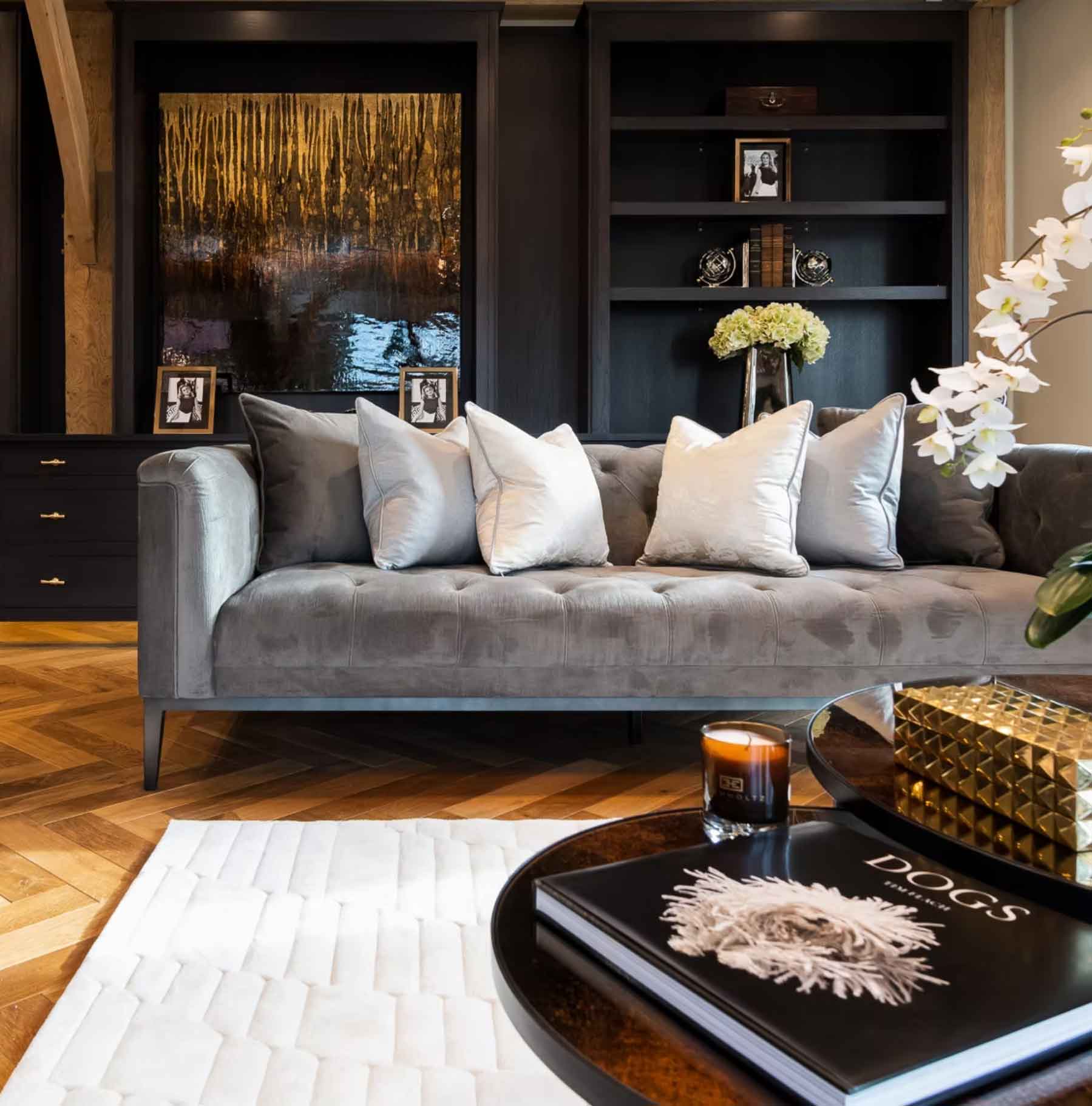 Luxury living room interior with grey velvet sofa, parquet flooring, dark built-in shelving, and elegant coffee table styling.