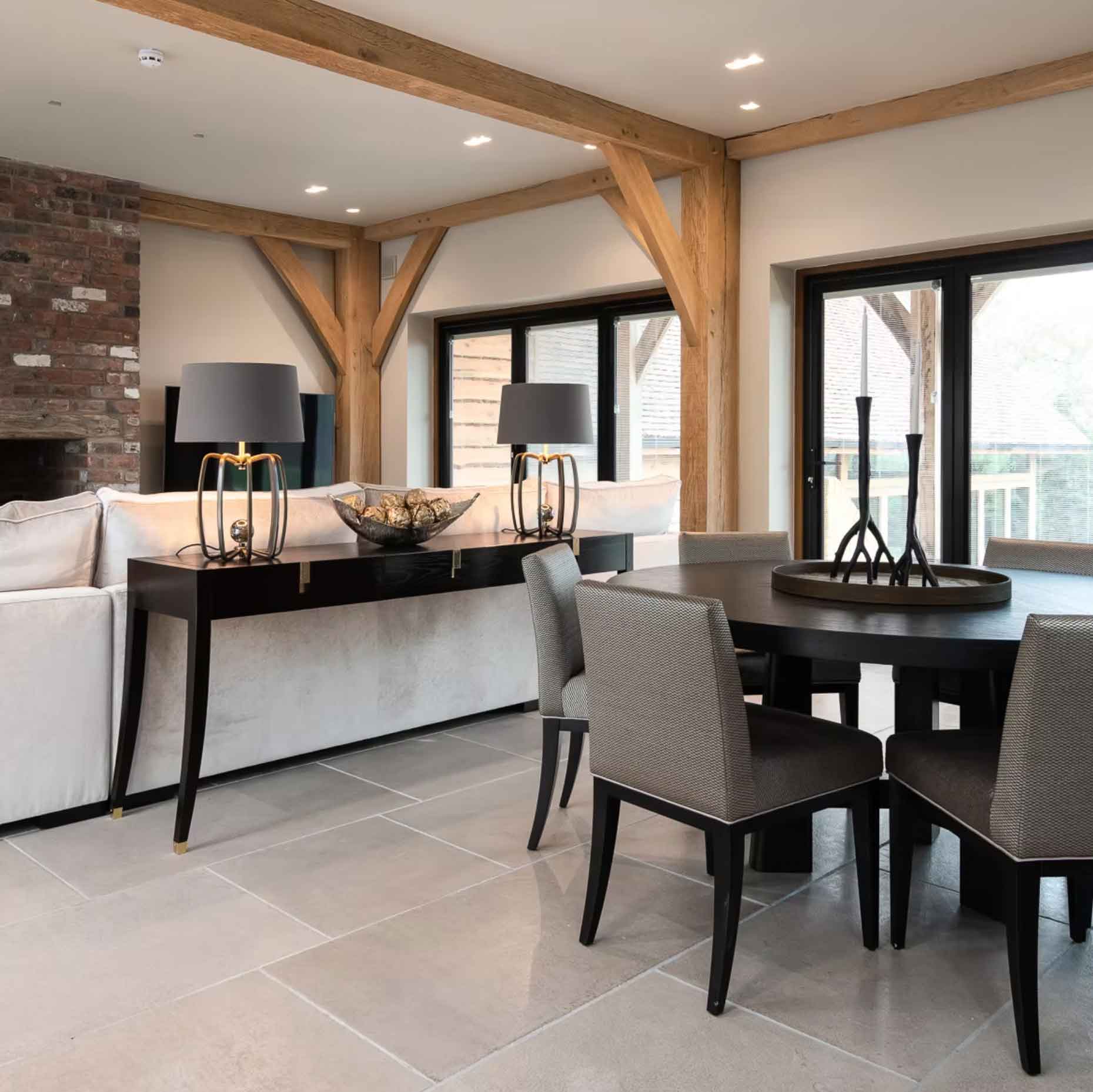 Contemporary dining area with oak beams, round table and neutral upholstered chairs – Kings Interiors, Oxfordshire interior design.