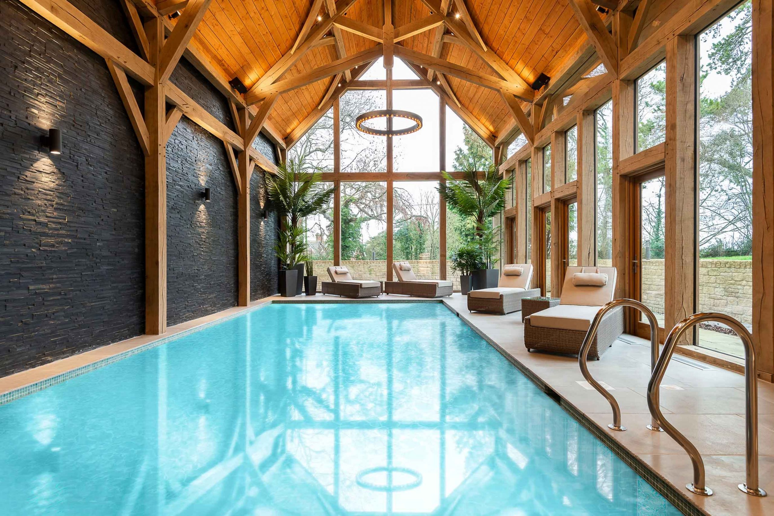 Indoor pool room with vaulted oak ceiling and slate feature wall – modern country home by Kings Interiors.