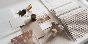 Curated interior materials palette with black and white marble, green stone, terrazzo, wood panels, and textured fabric samples in a warm studio setting.