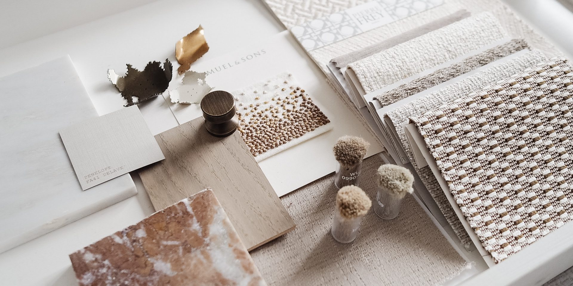 Curated interior materials palette with black and white marble, green stone, terrazzo, wood panels, and textured fabric samples in a warm studio setting.