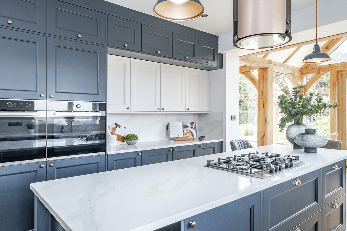 Luxury modern kitchen with navy shaker cabinets, white quartz island countertop, built-in double ovens, gas cooktop, and contemporary pendant lighting.