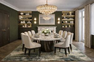 Photorealistic luxury dining room CGI render featuring an oval marble dining table, neutral upholstered chairs, dark olive green textured walls, marble fireplace with mirror, crystal chandelier and bespoke illuminated joinery.