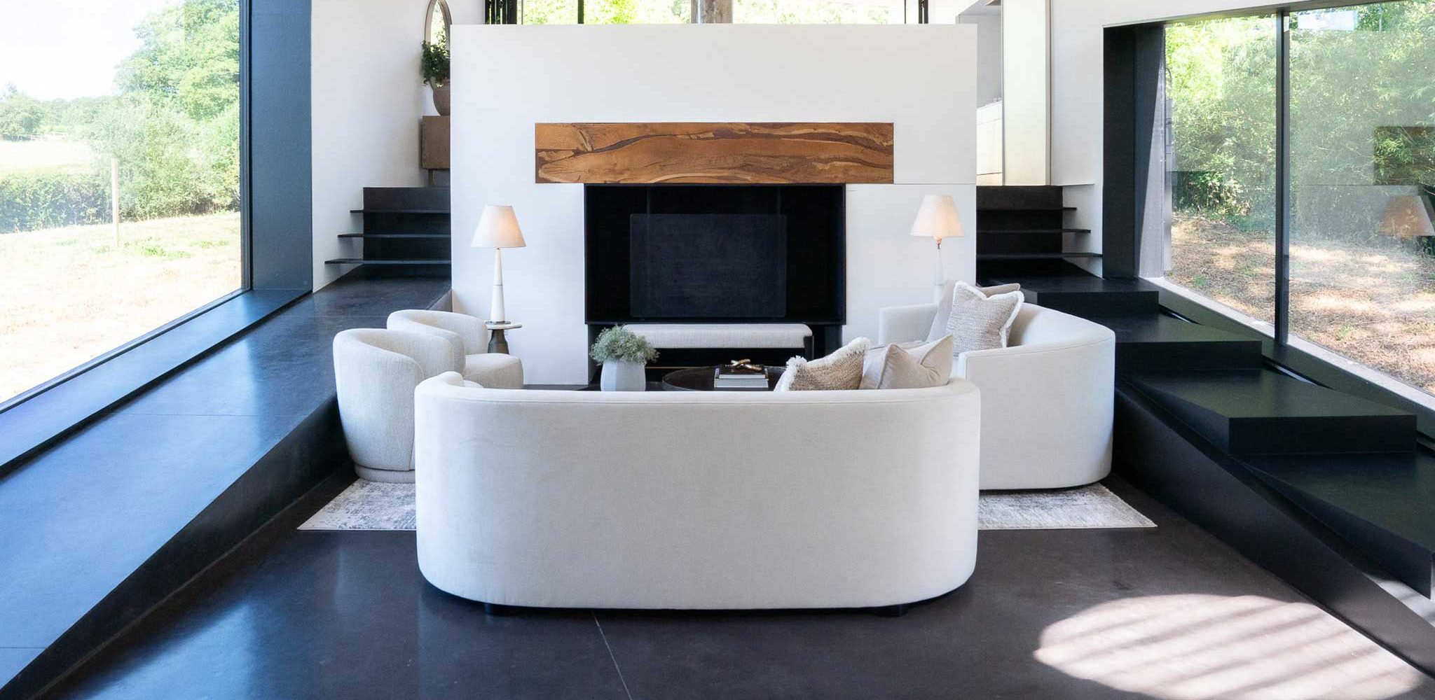Contemporary living room with curved cream sofas arranged around a fireplace.